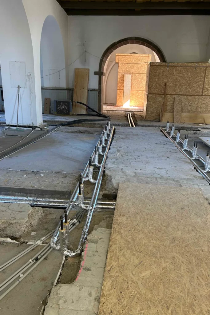 VVS-rør og fordelingsarrangement til midterbænke under gulvet i Nørresundby Kirke