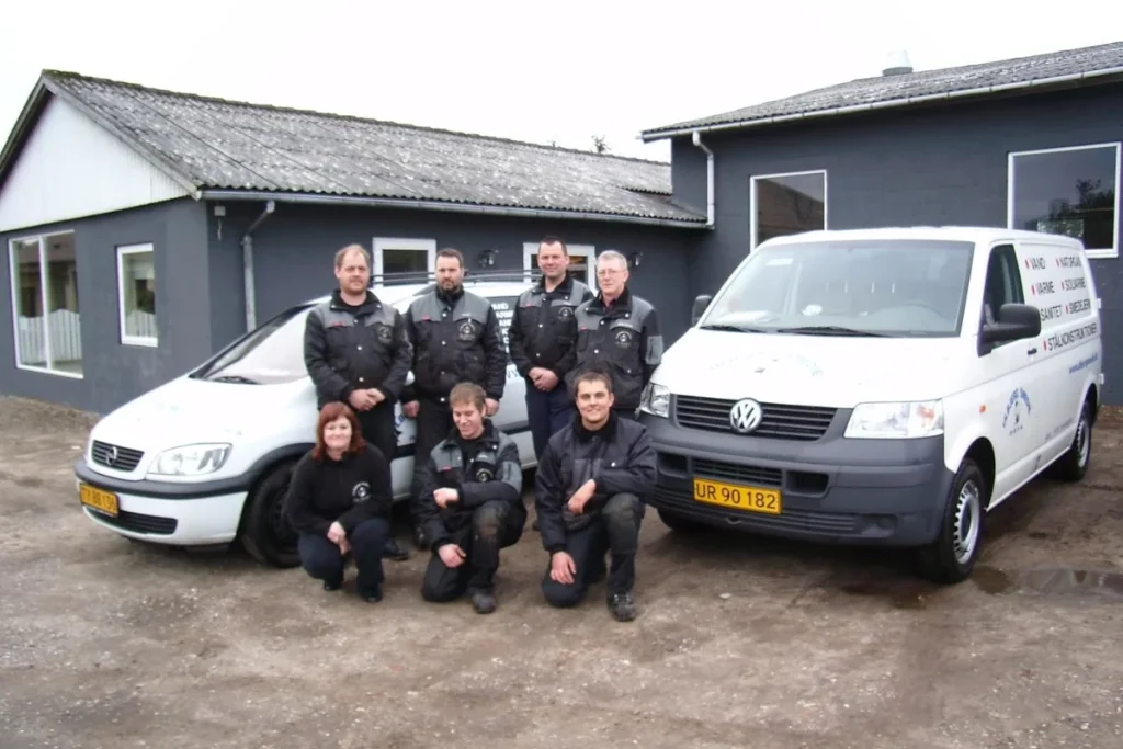 Medarbejdere fra Ulbjerg VVS foran virksomhedens bygning sammen med to servicebiler.